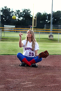 woman sitting in ballpark throwing softball