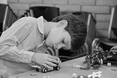grayscale photo of a boy wearing pinstriped button-up long-sleeved dress shirt vehicle plastic toy on table