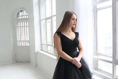 photo of woman wearing black plunging sleeveless dress standing near window
