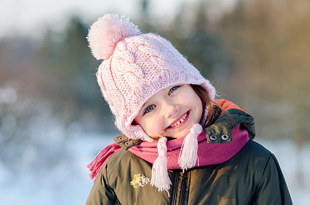 girl in green thermal jacket with pink pompom knit cap smiling