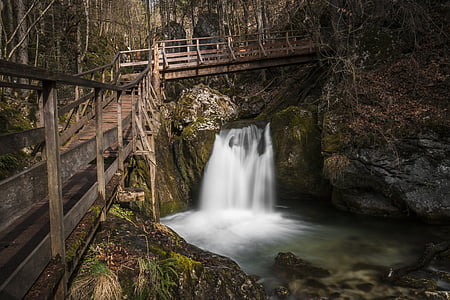 time lapse photo of waterfalls under brown wooden bridge during daytime