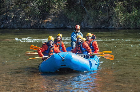 four smiling people wearing life vest riding on inflatable boat during daytime