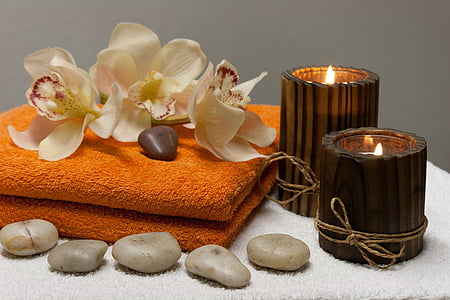 white orchids and two brown candles on top of orange towel closeup photography