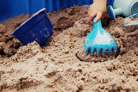 person holding blue plastic sand rake beside bucket on white sand
