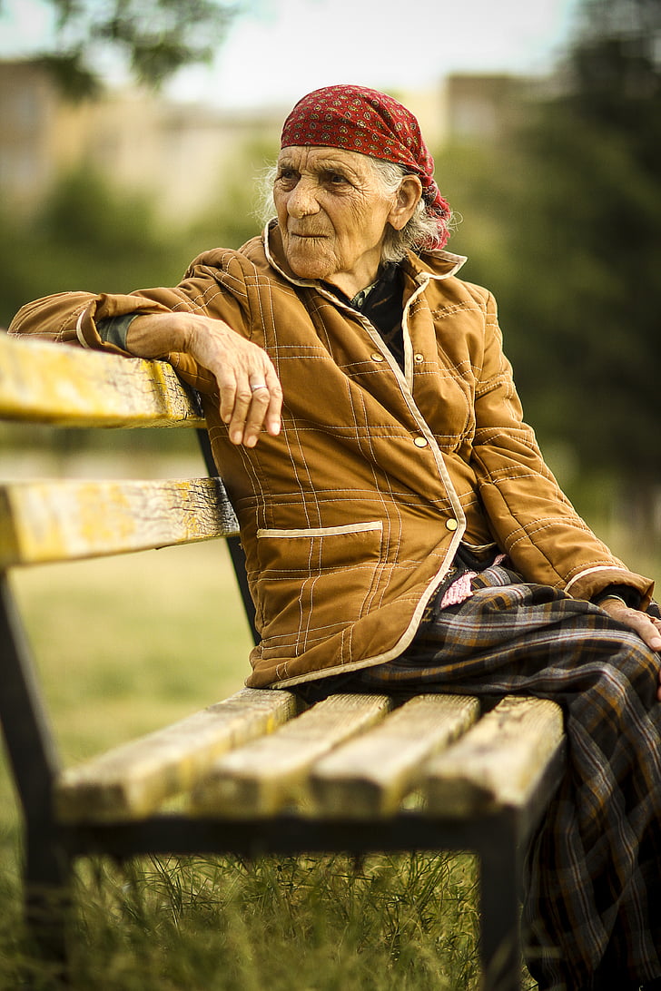 woman wearing brown jacket sitting on brown wooden bench