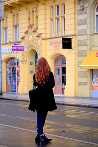 woman standing beside asphalt road and buildings