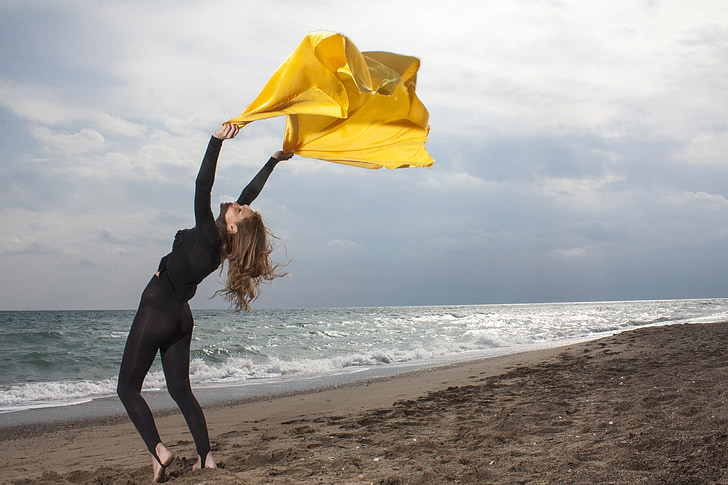 photo of woman in black wetsuit swaying yellow scarf