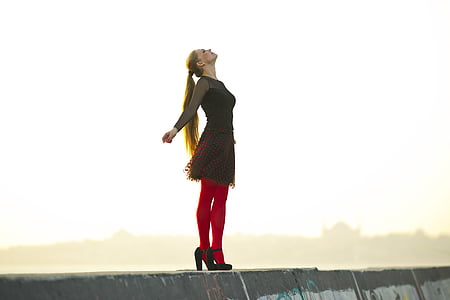 woman wearing black dress and red stockings standing on concrete platform during daytime