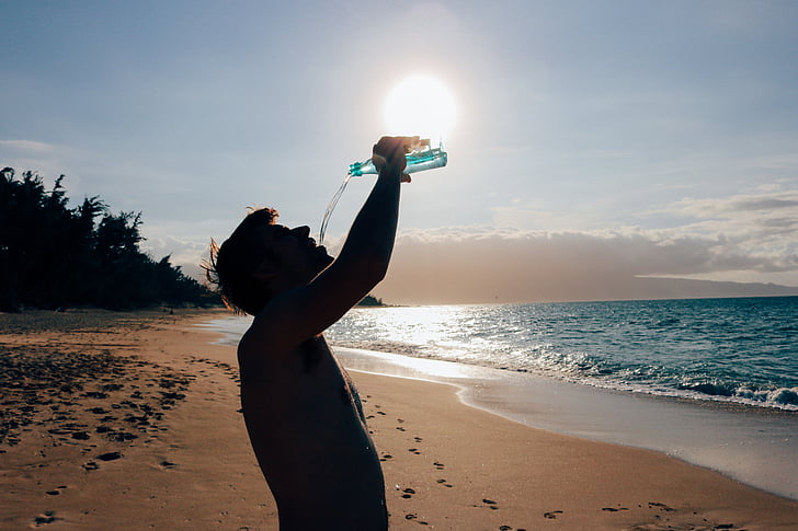 man holding bottle on seashore near body of water