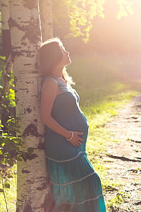 pregnant woman wearing blue maxi dress leaning on tree