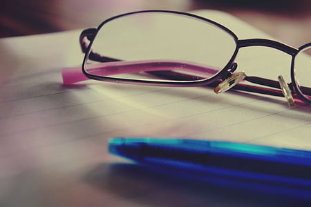 shallow focus photography of eyeglasses beside blue ballpoint pen
