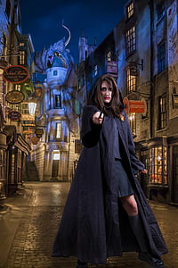 photo of woman wearing black hoodie coat holding black wand standing beside concrete buildings