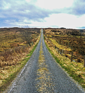 gray road between grassland during daytime