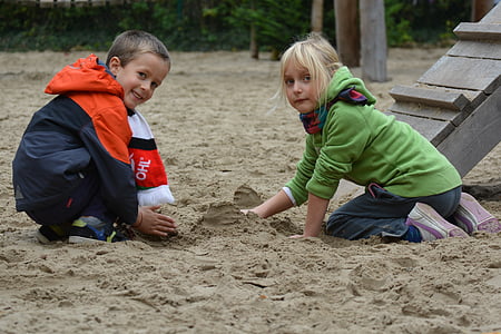 boy and girl playing on sand outdoors during daytime