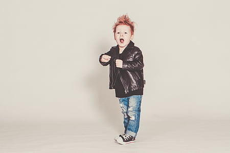 boy wearing black leather jacket and distressed blue denim jeans in room