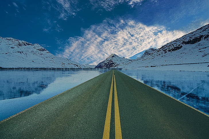 landscape photography of pavement road near body of water and snow covered mountain