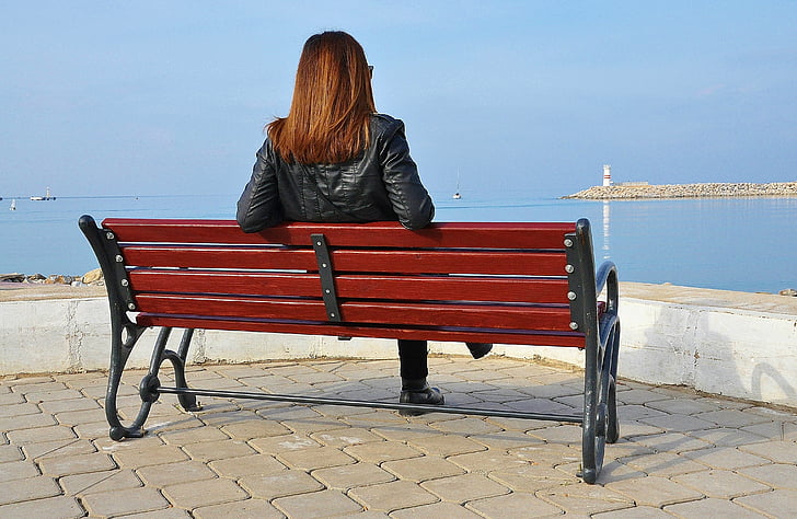 woman sitting on black and red wooden bench looking on wide open body of water