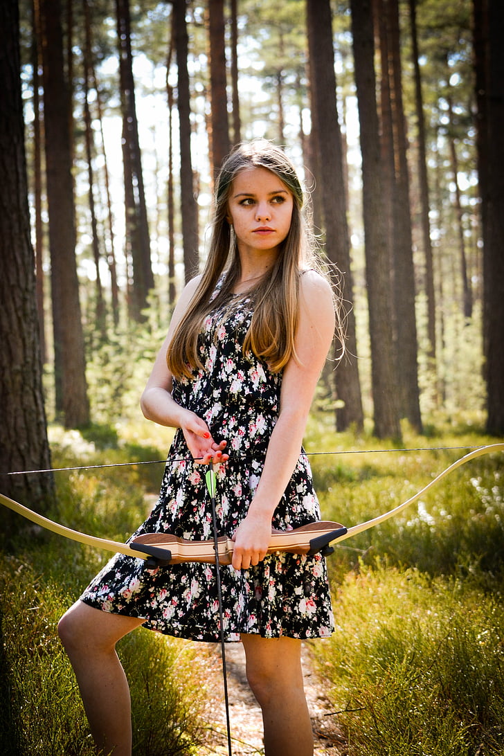 woman wearing tank mini dress holding composite bow and arrow in forest