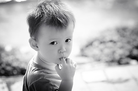 grayscale photography of boy wearing crew-neck shirt eating his finger