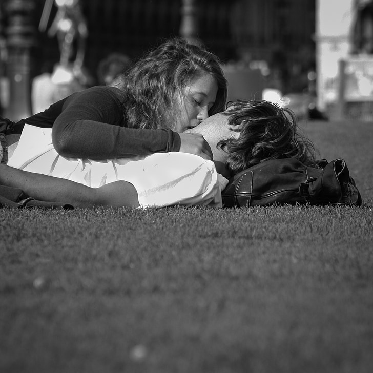 grayscale photo of man and woman kissing on field of grass