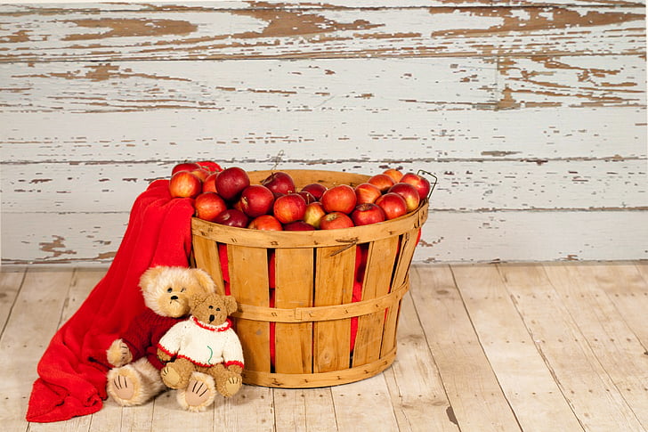 two brown bear plush toys leaning on brown wooden basket with red apple fruit lot