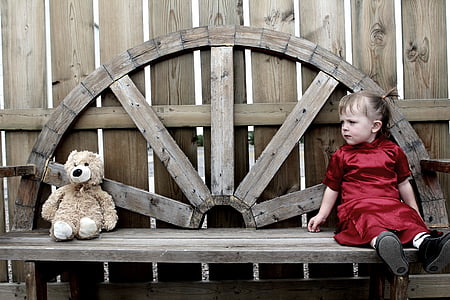 girl sitting on brown wooden bench while looking at brown bear plush toy