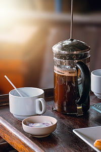 full filled coffee press beside coffee cup on brown wooden table