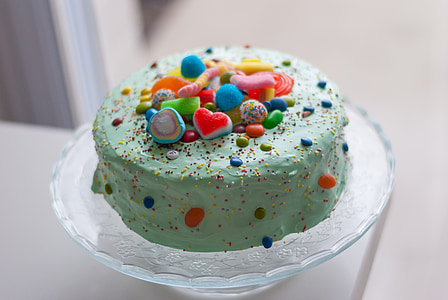 green icing-covered cake with multicolored toppings on glas cake dome