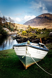 white and green wooden boat near calm grey body of water and mountain at daytime