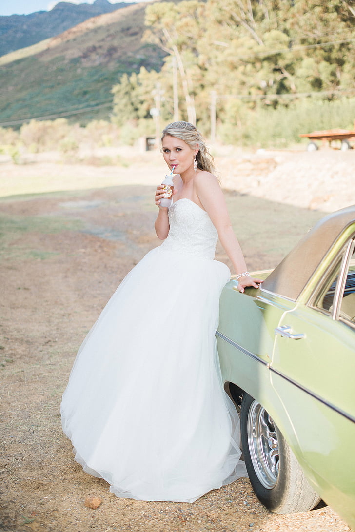 woman in white wedding dress sitting on car tailgate