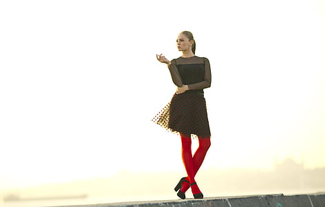 woman wears black long-sleeved dress with red leg stocking