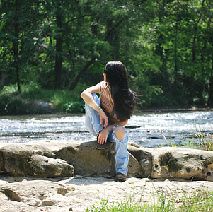 woman sitting on rock near body of water