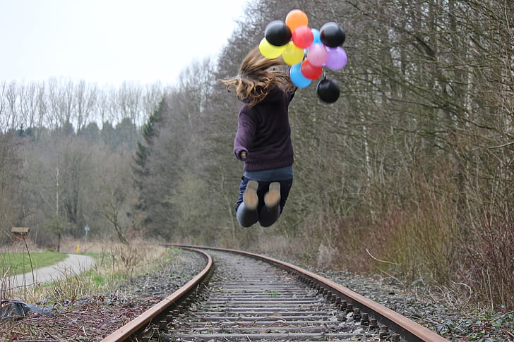 girl jumping on train track while holding balloons