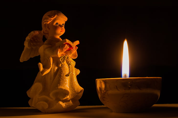 angel holding book figurine beside lighted candle