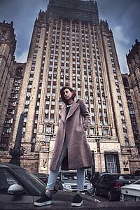 low angle photography of a woman in brown coat in front of building