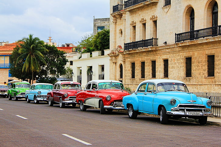 assorted-colored classic cars park on road beside black metal rails