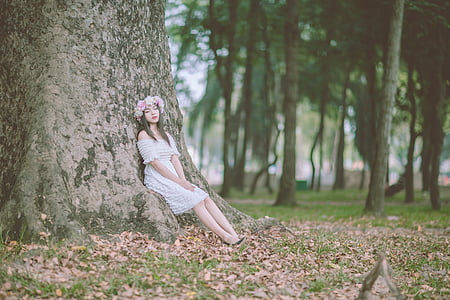 portrait photography of woman in white dress leaning on tree