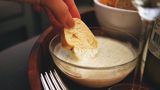 person holding sliced of bread dipped in cream with bowl
