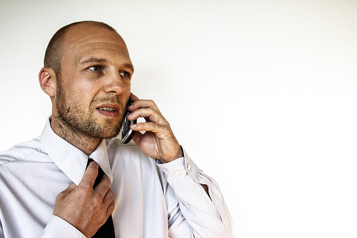 man holding his tie while talking to his phone