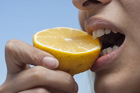 close photo of person biting yellow citrus fruit