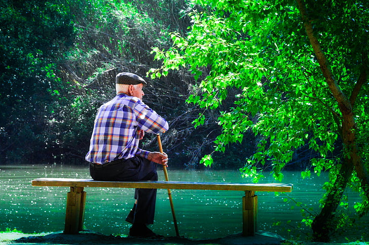 man sitting on bench facing body of water