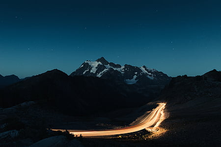 time lapse photography of road beside snow-capped mountain during night time