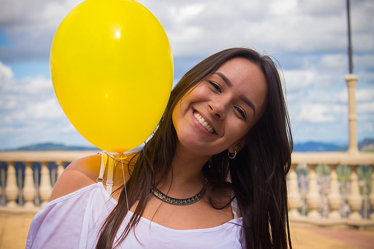 woman in white top holding yellow balloon