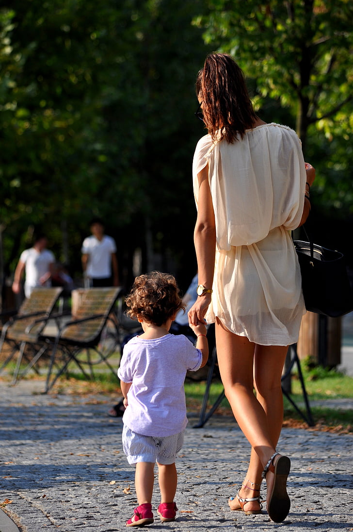 woman wearing white dress holding hand of toddler