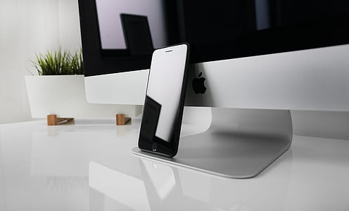 black iPhone leaned on silver iMac