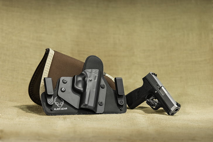 closeup photo of black and gray semi-automatic pistol beside brown and black leather and plastic holster placed on beige textile