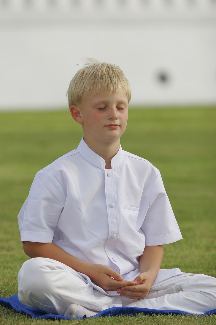 boy wearing white outfit while meditating on green grass field