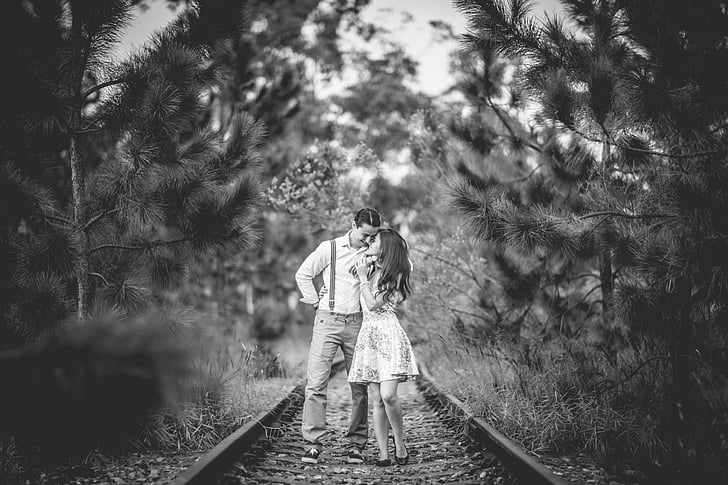 grayscale photography of man and woman standing on train rails