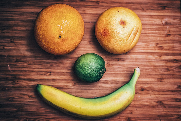 two oranges, one lemon, and banana forming a smile on brown wooden surface