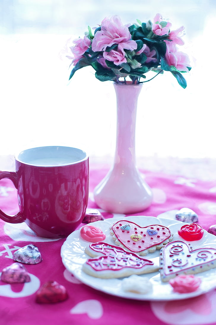 pink petaled flowers with white ceramic vase beside red ceramic mug